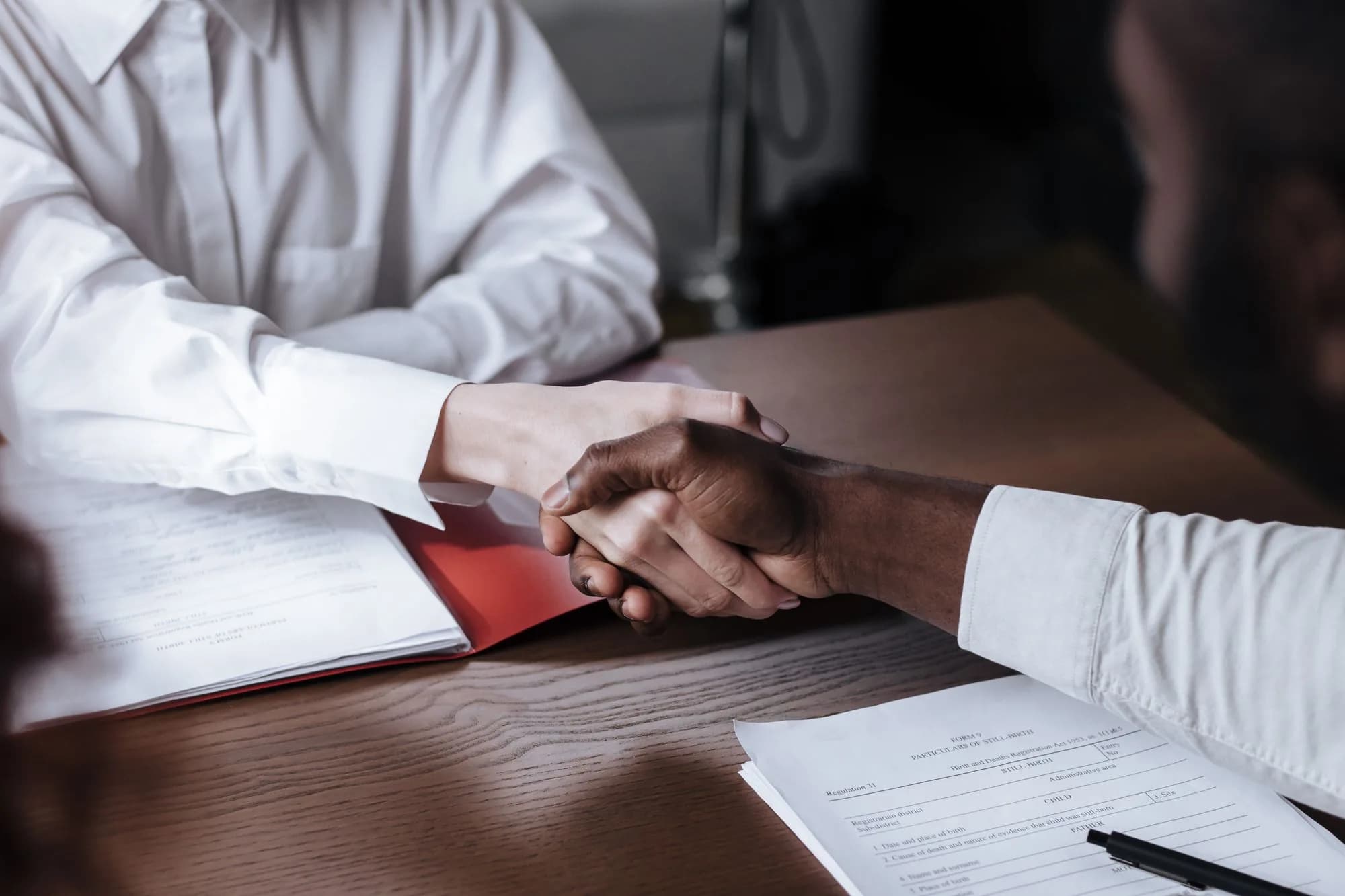 Two people shaking hands over signed documents